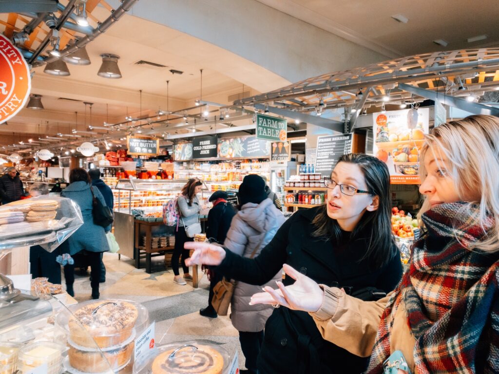 Two young millennials having a conversation about pastries in the marketplace of grand central termi